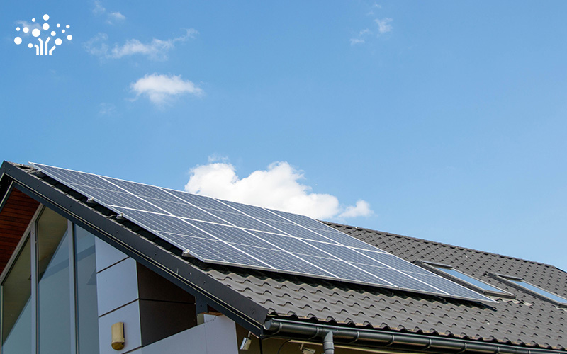 Residential building with solar panels arranged in a grid on the sloped roof under a partly cloudy sky.