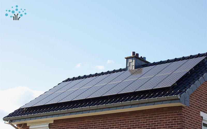 Solar panels installed in grid pattern on sloped roof of brick house under sunny sky with clouds