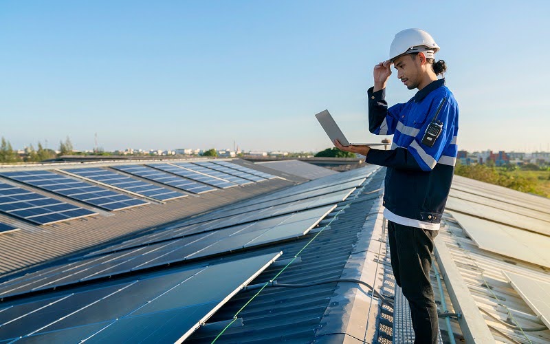 Engineer using laptop to inspect industrial rooftop solar panels.
