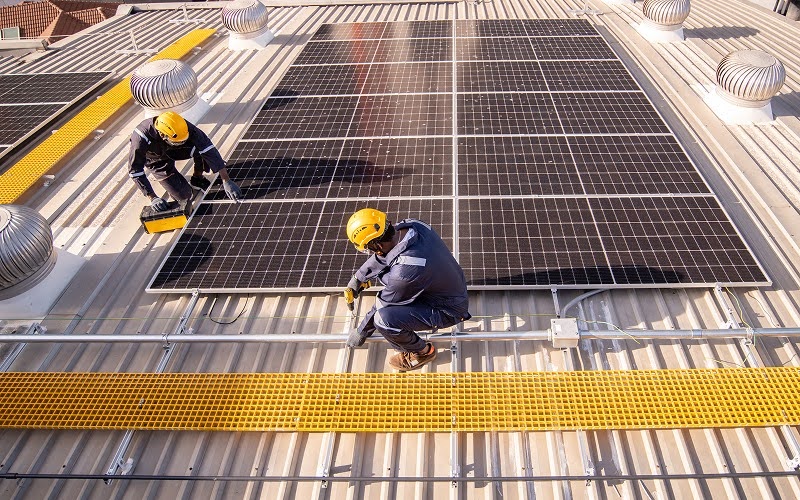 Technicians installing solar panel system on industrial warehouse roof.